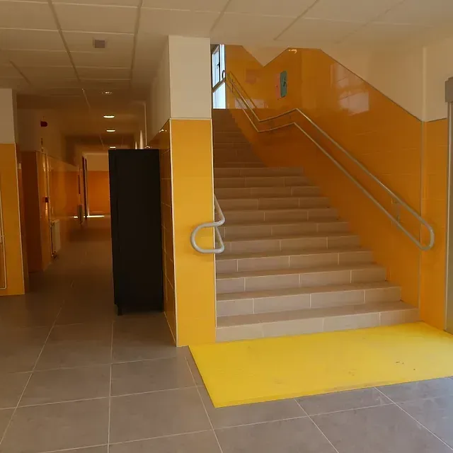 Pasillo con paredes y escaleras amarillas, un armario oscuro y suelo gris.