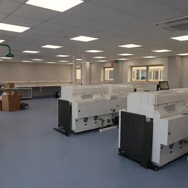 Un laboratorio vacío con máquinas automatizadas, paredes blancas, piso azul e iluminación cenital.