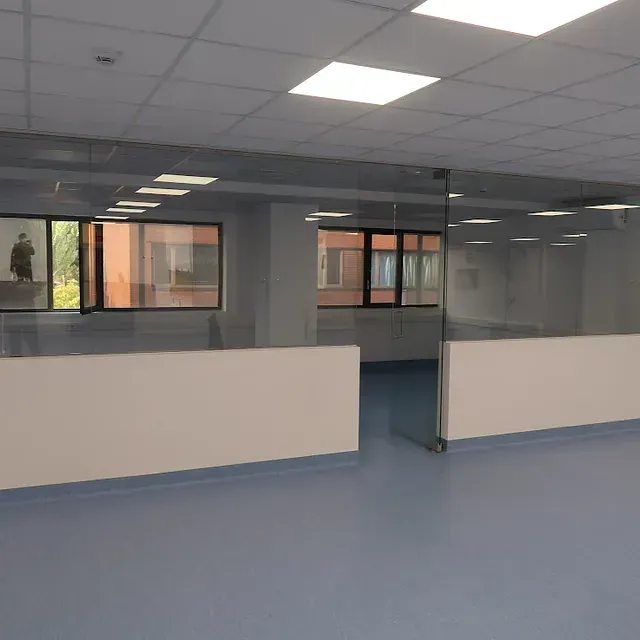 Espacio de oficina vacío con piso azul, paredes blancas, mampara de vidrio y ventanas.