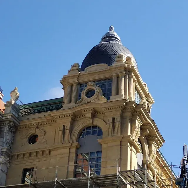 Edificio beige con una cúpula azul oscuro, arquitectura ornamentada y un cielo azul claro.