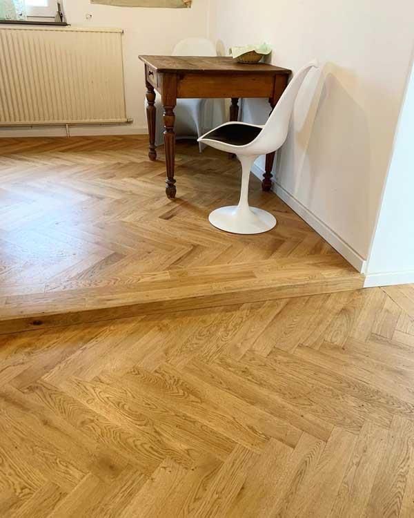 Ein Holzboden mit Fischgrätenmuster sowie ein Tisch und Stuhl.