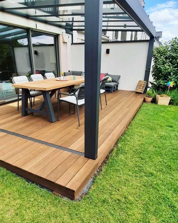 Eine Holzterrasse mit Tisch und Stühlen unter einer Pergola.