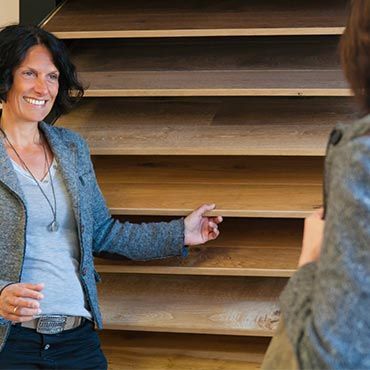 Eine Frau steht vor einer Holztreppe und unterhält sich mit einer anderen Frau.