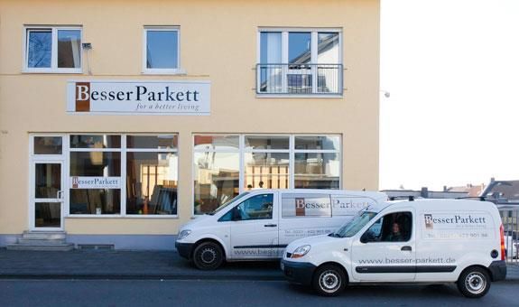 Zwei weiße Lieferwagen stehen vor einem Gebäude mit der Aufschrift „besser parkett“