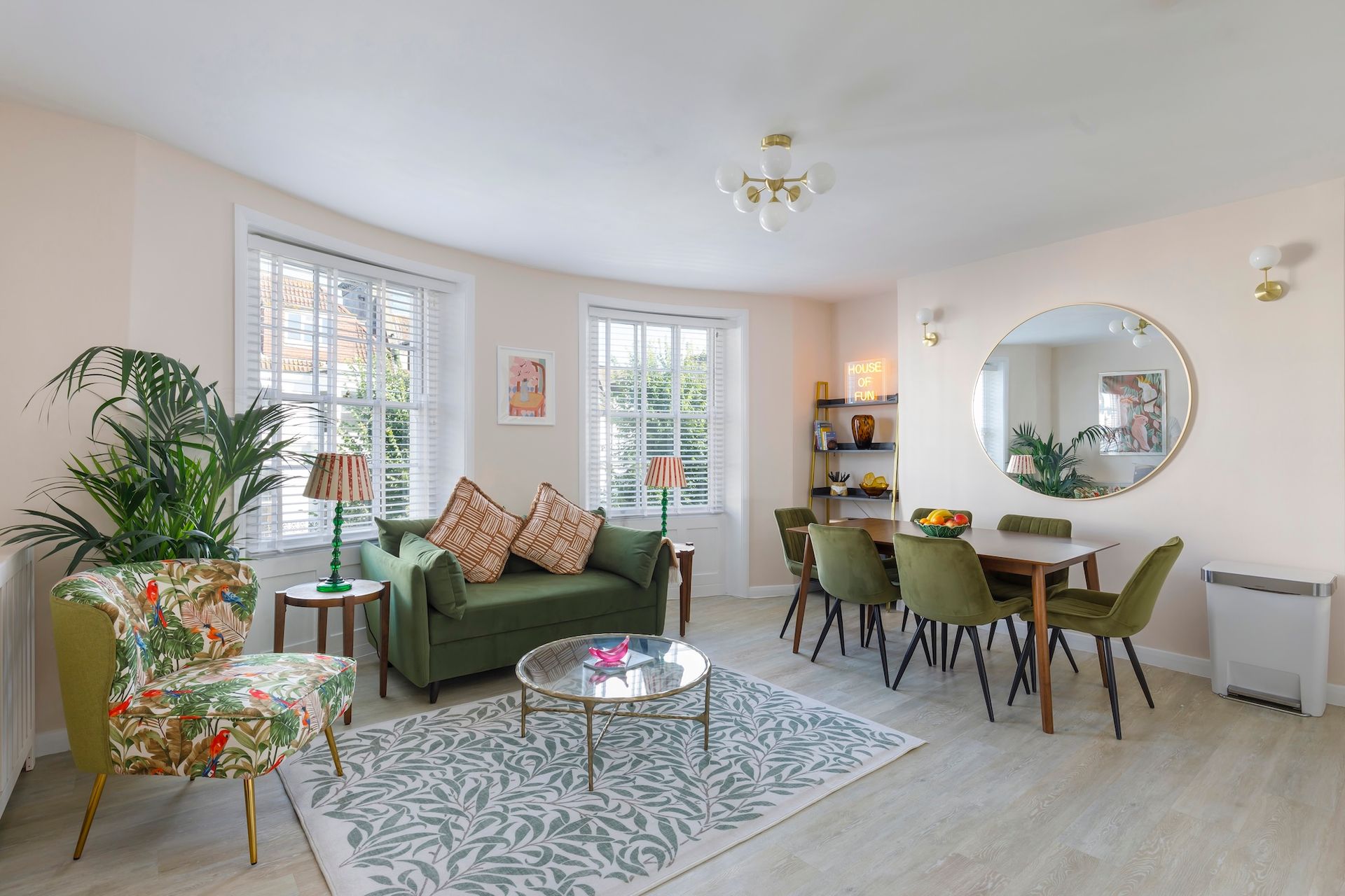 A living room with a green couch , chairs , a table and a mirror.