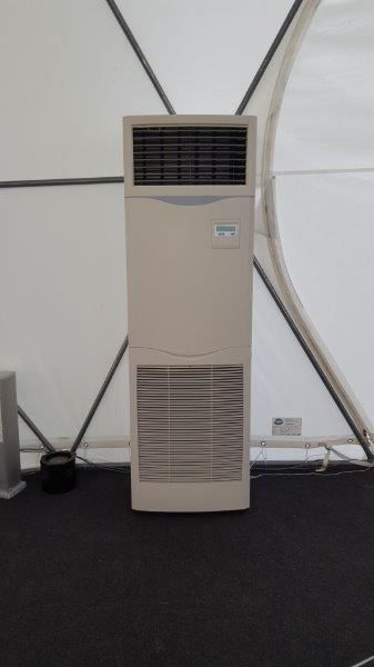 Unité de climatisation beige de grande taille, placée dans une tente blanche sur un sol sombre.