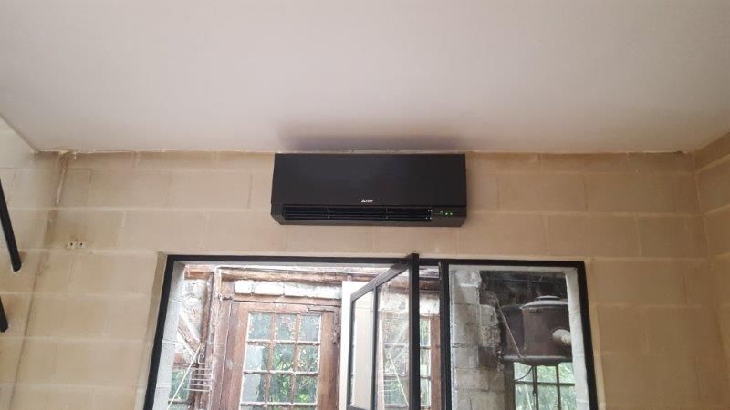 Climatiseur noir fixé sur un mur beige au-dessus d'une fenêtre.