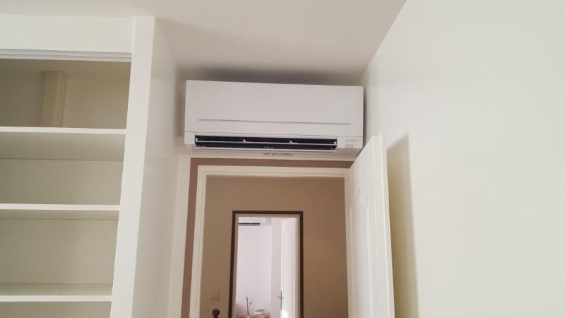 Unité de climatisation blanche fixée au-dessus d'une porte, à côté d'une bibliothèque intégrée.