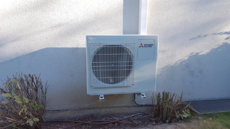 Climatiseur Mitsubishi blanc fixé sur un mur en stuc à l'extérieur d'un bâtiment.