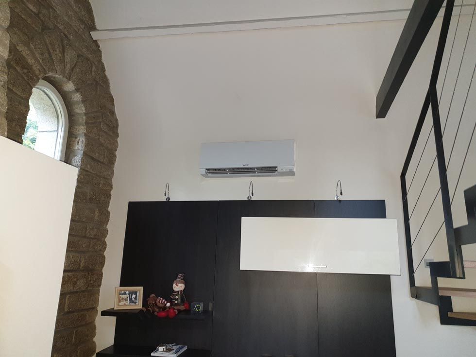 Intérieur avec murs blancs, une armoire noire, un escalier, une fenêtre cintrée et un climatiseur.