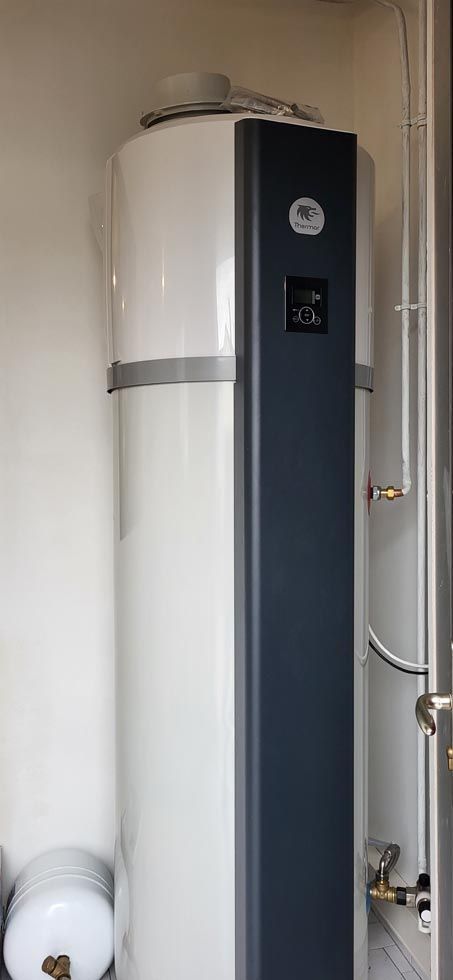 Réservoir d'eau chaude blanc et gris avec panneau de commande, installé contre un mur blanc.