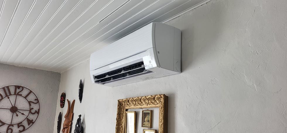 Unité de climatisation blanche fixée sur un mur texturé, avec une horloge décorative et un miroir en dessous.
