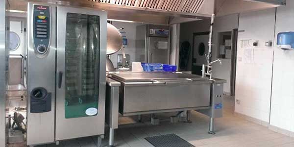 Cuisine professionnelle équipée d'appareils en acier inoxydable : four, plaque de cuisson et hotte.