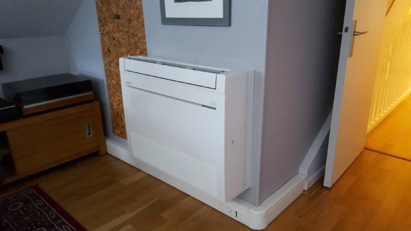 Unité de climatisation blanche sur un mur gris dans une pièce au parquet.