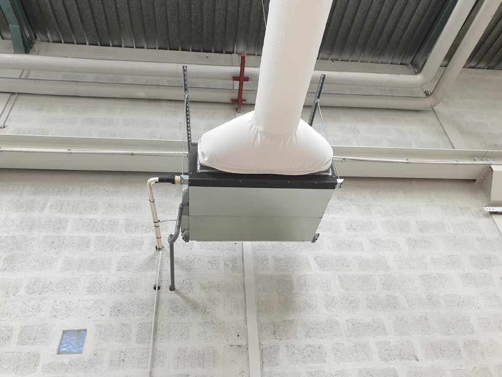 Unité de climatisation métallique fixée à un mur en briques de béton avec un conduit et des tuyaux blancs.