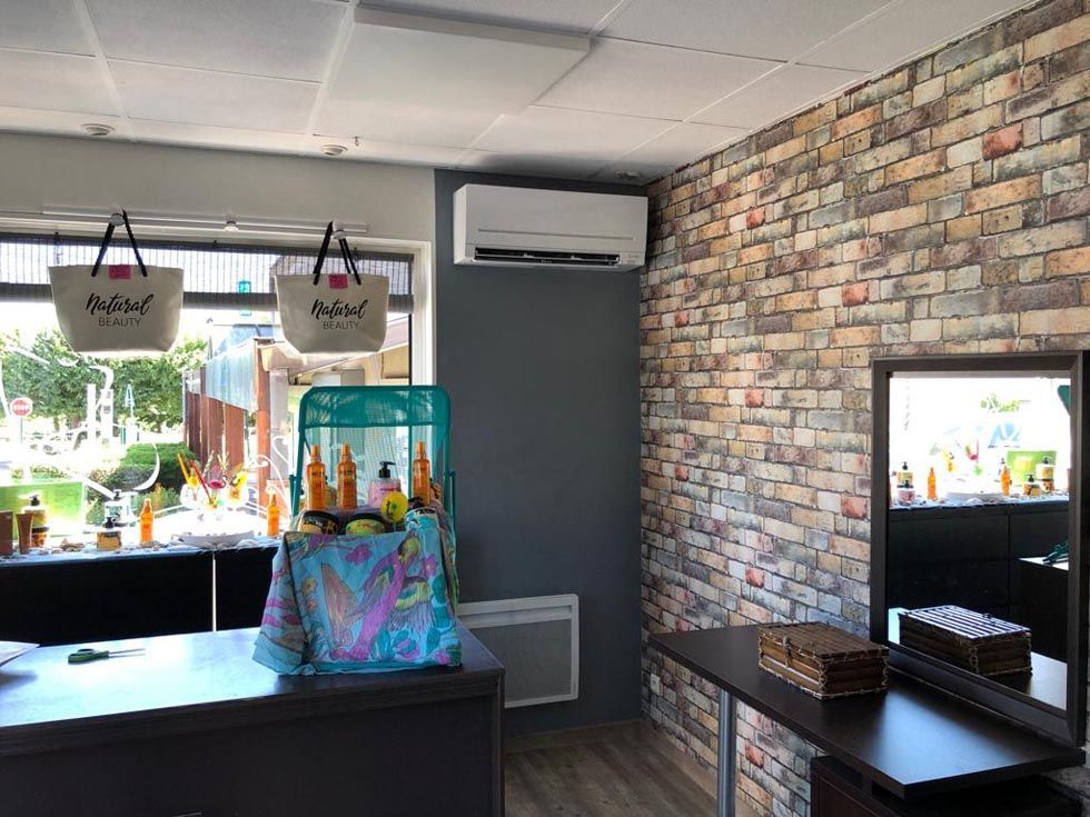 Intérieur d'un magasin avec un mur de briques, un grand miroir, une table et des sacs suspendus aux vitrines.