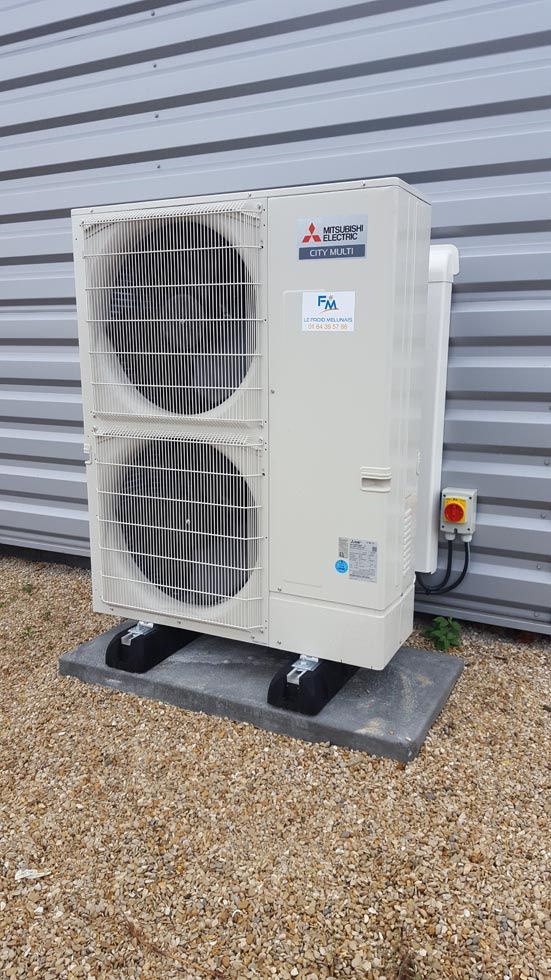 Unité de climatisation Mitsubishi sur une dalle de béton à l'extérieur d'un bâtiment au revêtement gris.