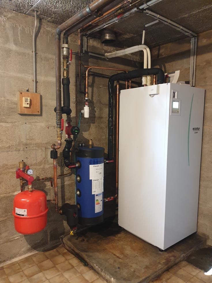 Unité de chauffage blanche, ballon bleu et réservoir rouge avec tuyauterie en cuivre, le tout installé dans un sous-sol.