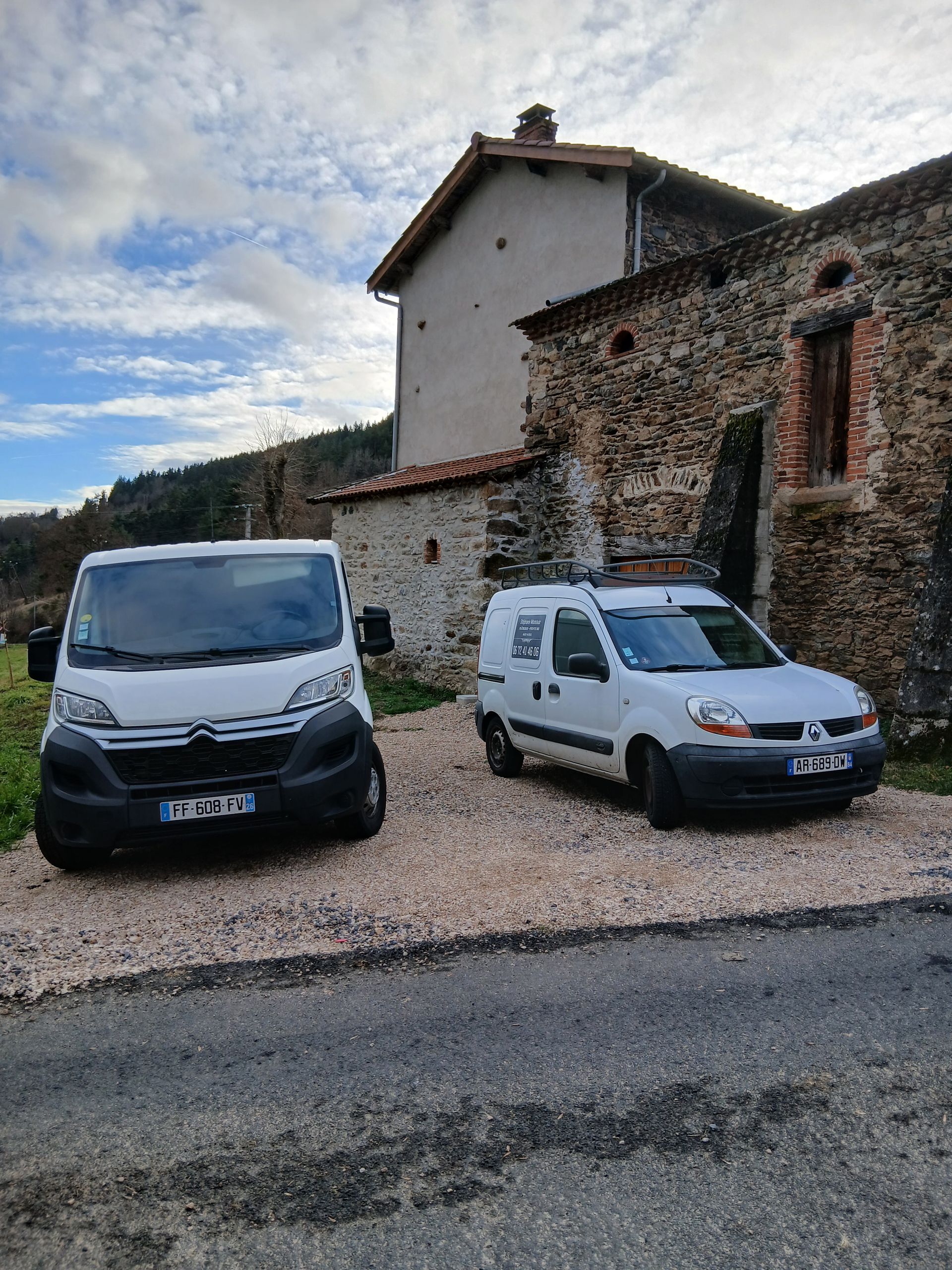 Deux camionnettes blanches garées sur du gravier près d'un bâtiment en pierre sous un ciel nuageux.