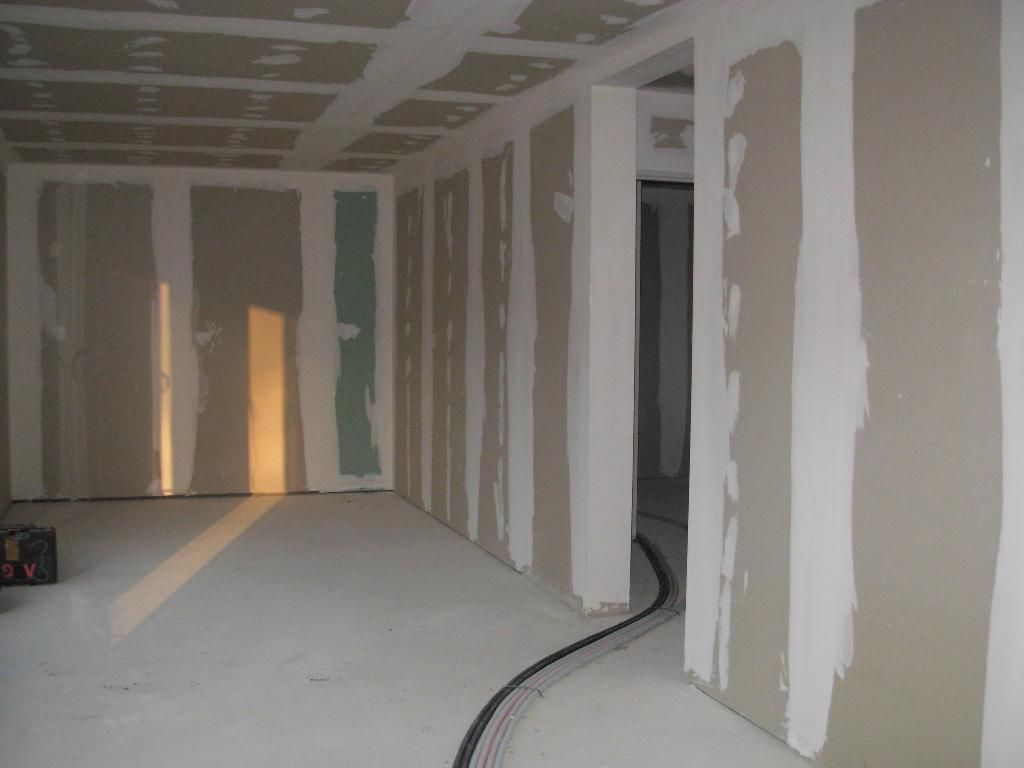 Intérieur d'une pièce en construction, cloisons sèches posées, joints collés et enduits, teintes grises et blanches.