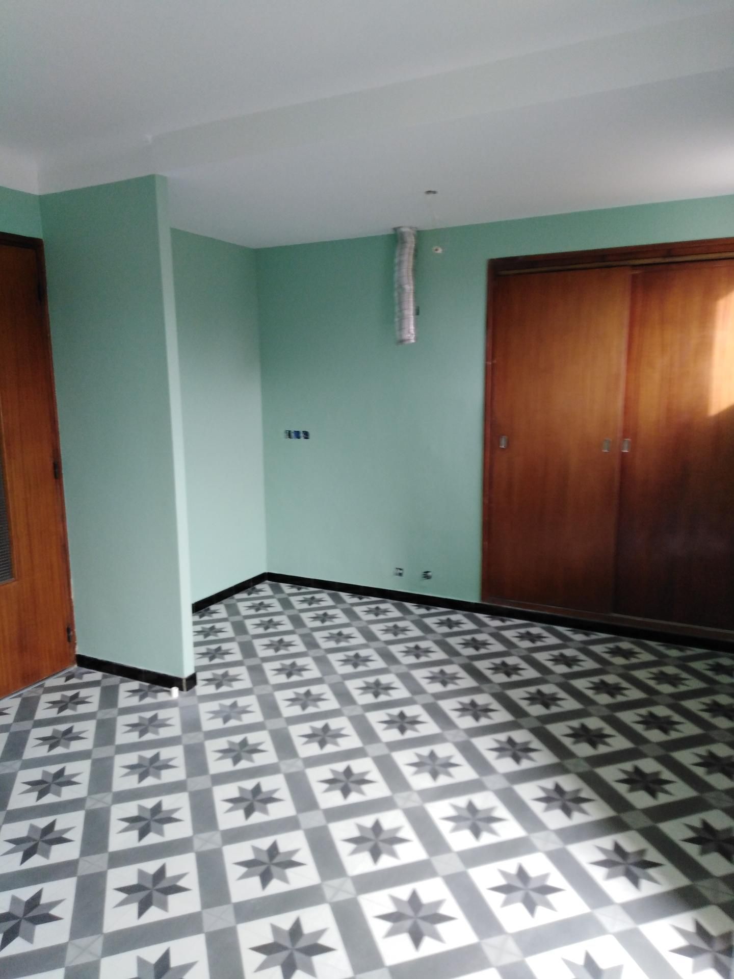 Pièce vide aux murs verts, portes et placard en bois, sol à motifs.