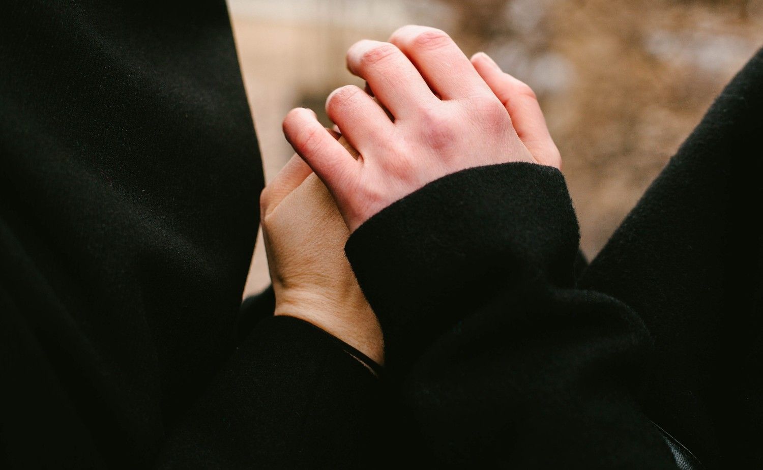 Dos personas se toman de la mano, con los dedos entrelazados, y visten ropa oscura.