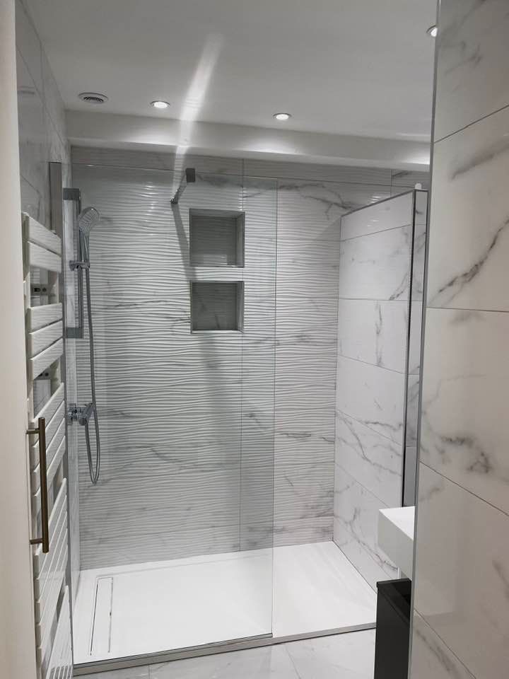 Salle de bains avec carrelage imitation marbre, douche en verre, étagères intégrées et sèche-serviettes.