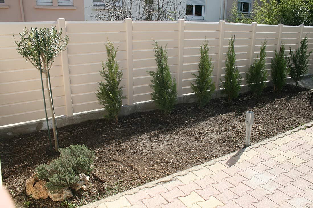Alignement de plusieurs petits arbustes le long d'une clôture en PVC blanche