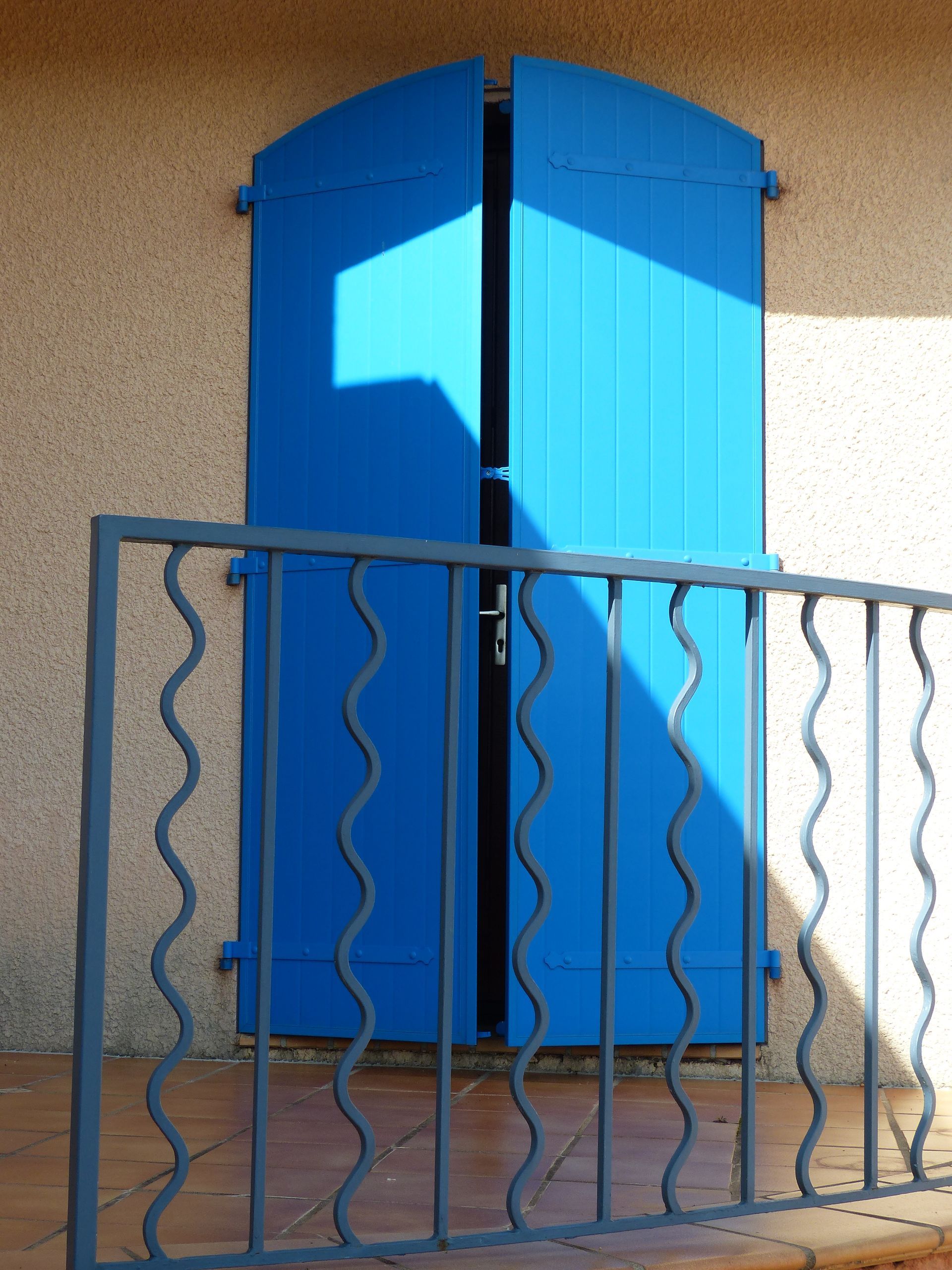 Volets battants bleus entrouverts à un balcon