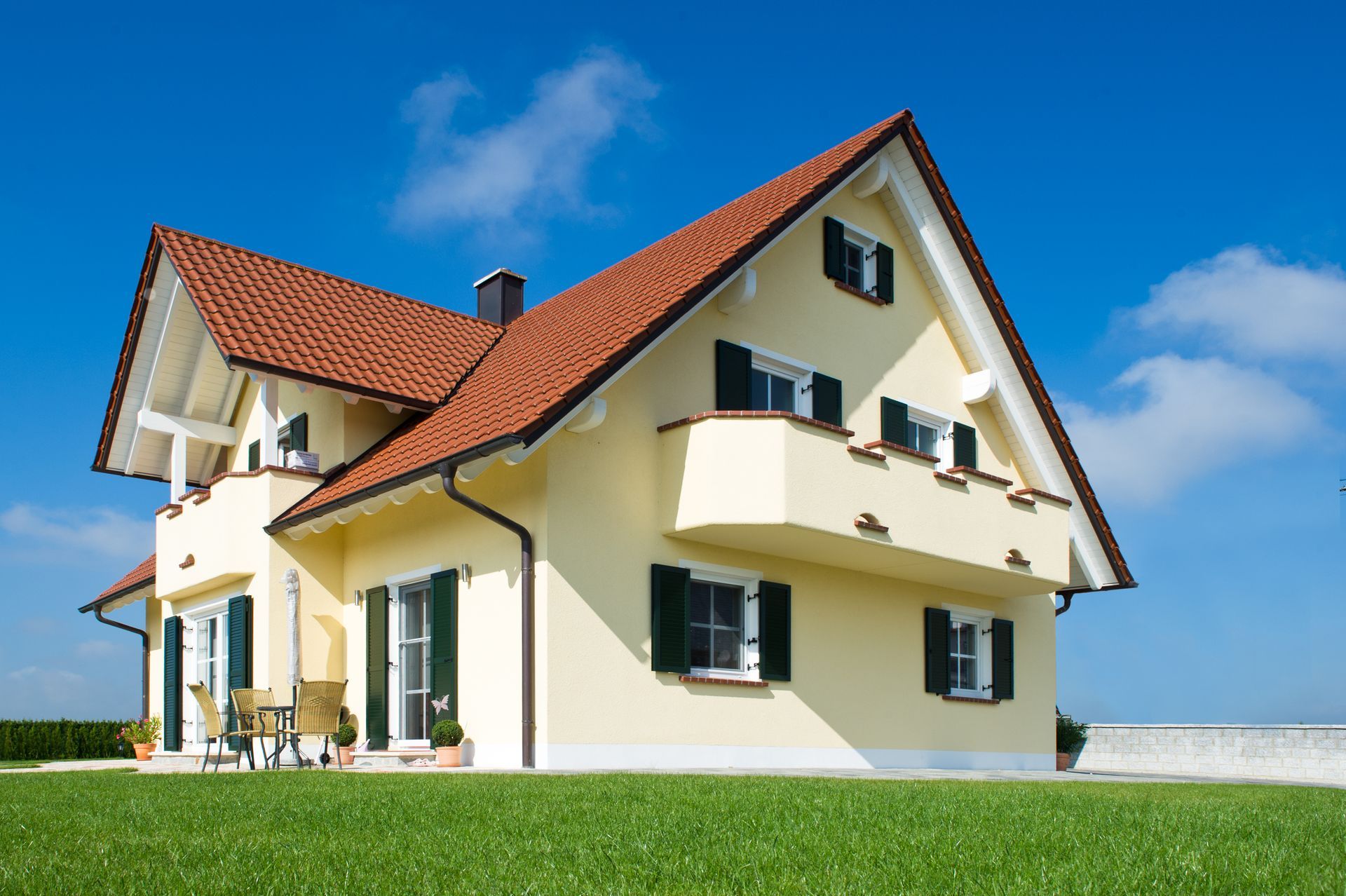 Edificio moderno con persiane grigie chiuse sopra una finestra e una porta scorrevole, accanto a una terrazza in legno.