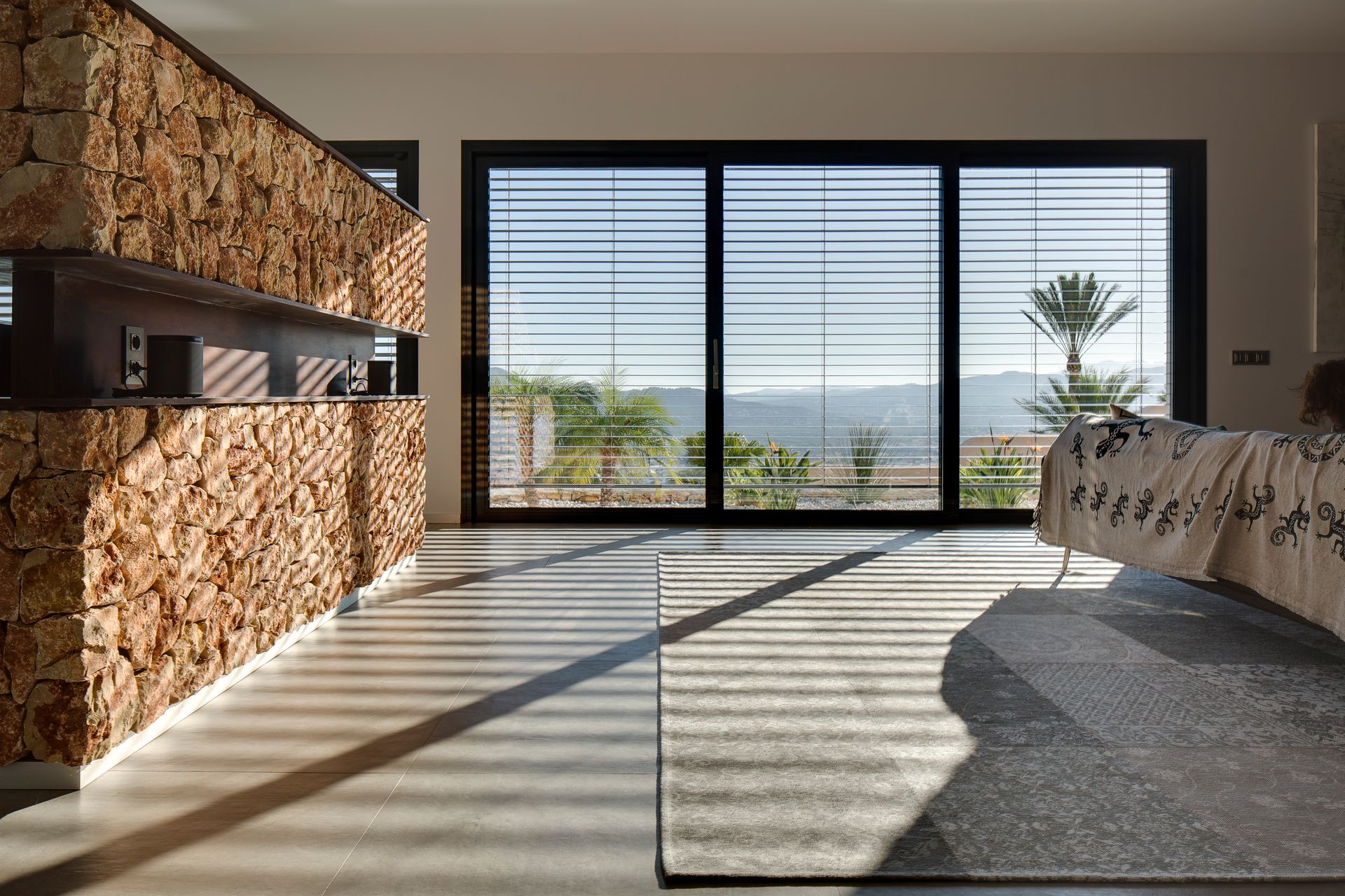 Soggiorno con porta scorrevole in vetro, tende orizzontali, pavimento in legno chiaro, divano bianco e camino.