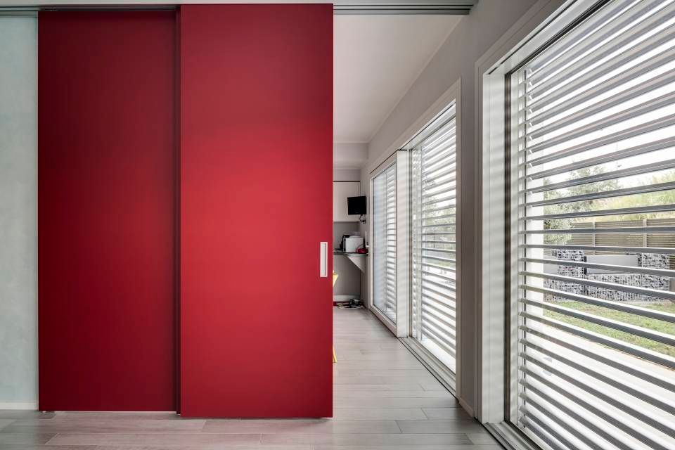 Le porte scorrevoli rosse si aprono su una stanza luminosa, dotata di tende e lavatrice.