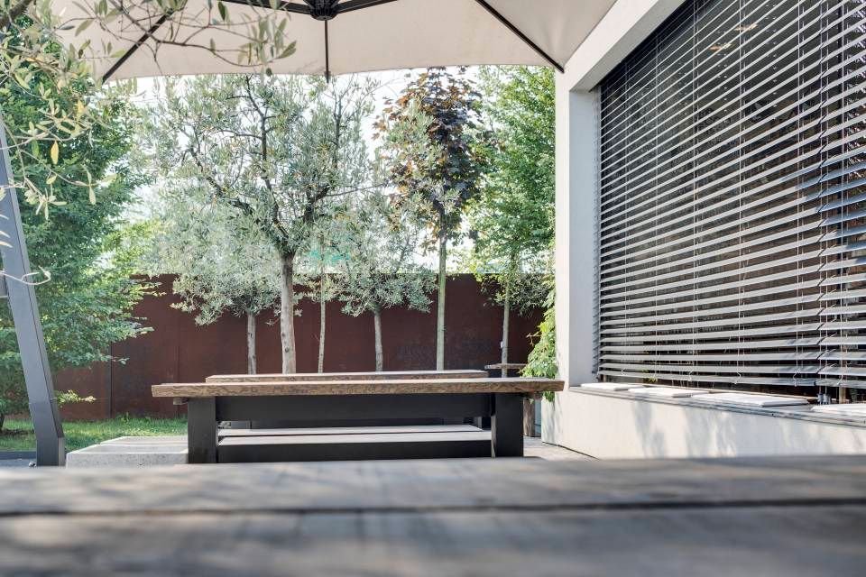 Panca di legno su un patio, con alberi e un edificio moderno sullo sfondo.