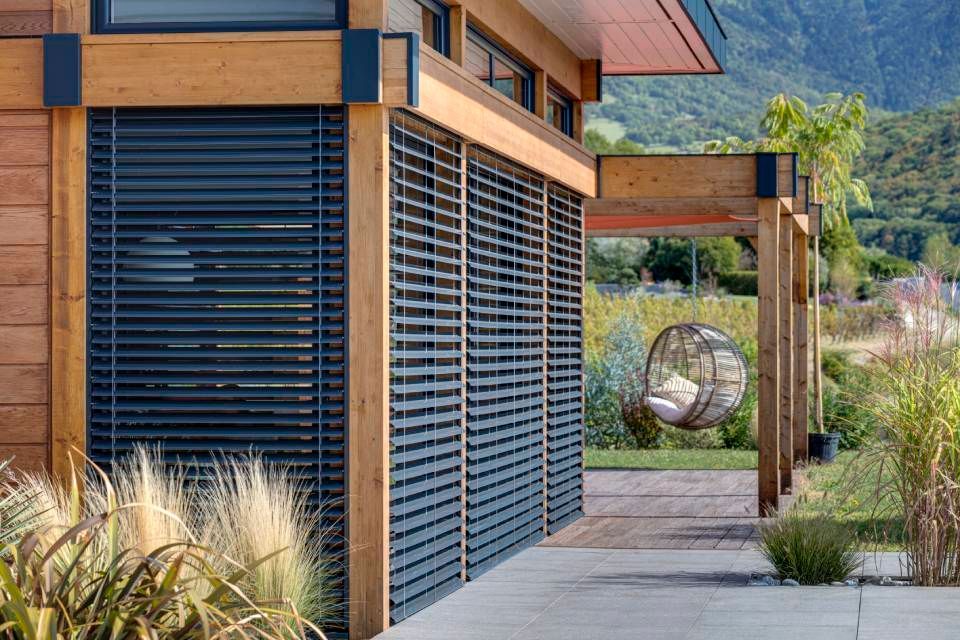 Edificio in legno con persiane scure, area salotto all'aperto e giardino lussureggiante.