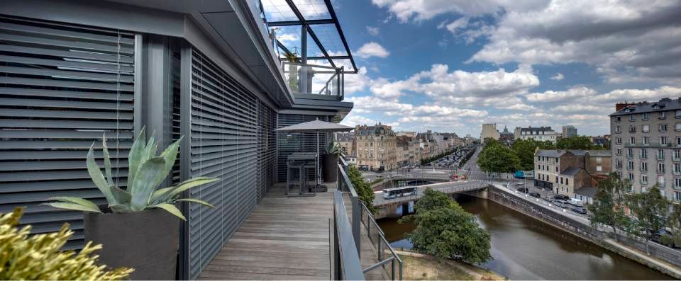 Un balcone moderno con piante che si affaccia su un paesaggio urbano con un fiume, ponti ed edifici sotto un cielo nuvoloso.