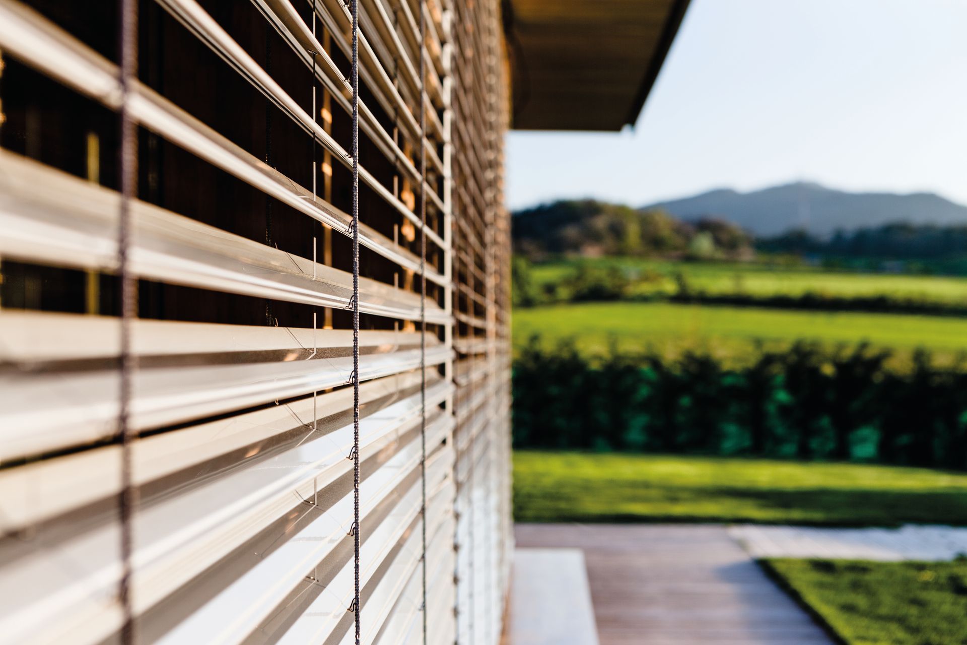 Persiane in legno sulla facciata esterna di un edificio, disposte ad angolo con un paesaggio verde sfocato sullo sfondo.