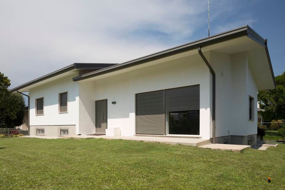 Casa bianca con tetto e finiture grigio scuro, prato verde, cielo limpido.
