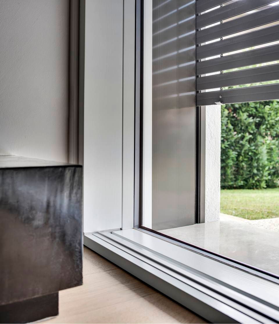 Finestra con persiane orizzontali chiuse; attraverso la finestra si vede un patio e un prato verde.