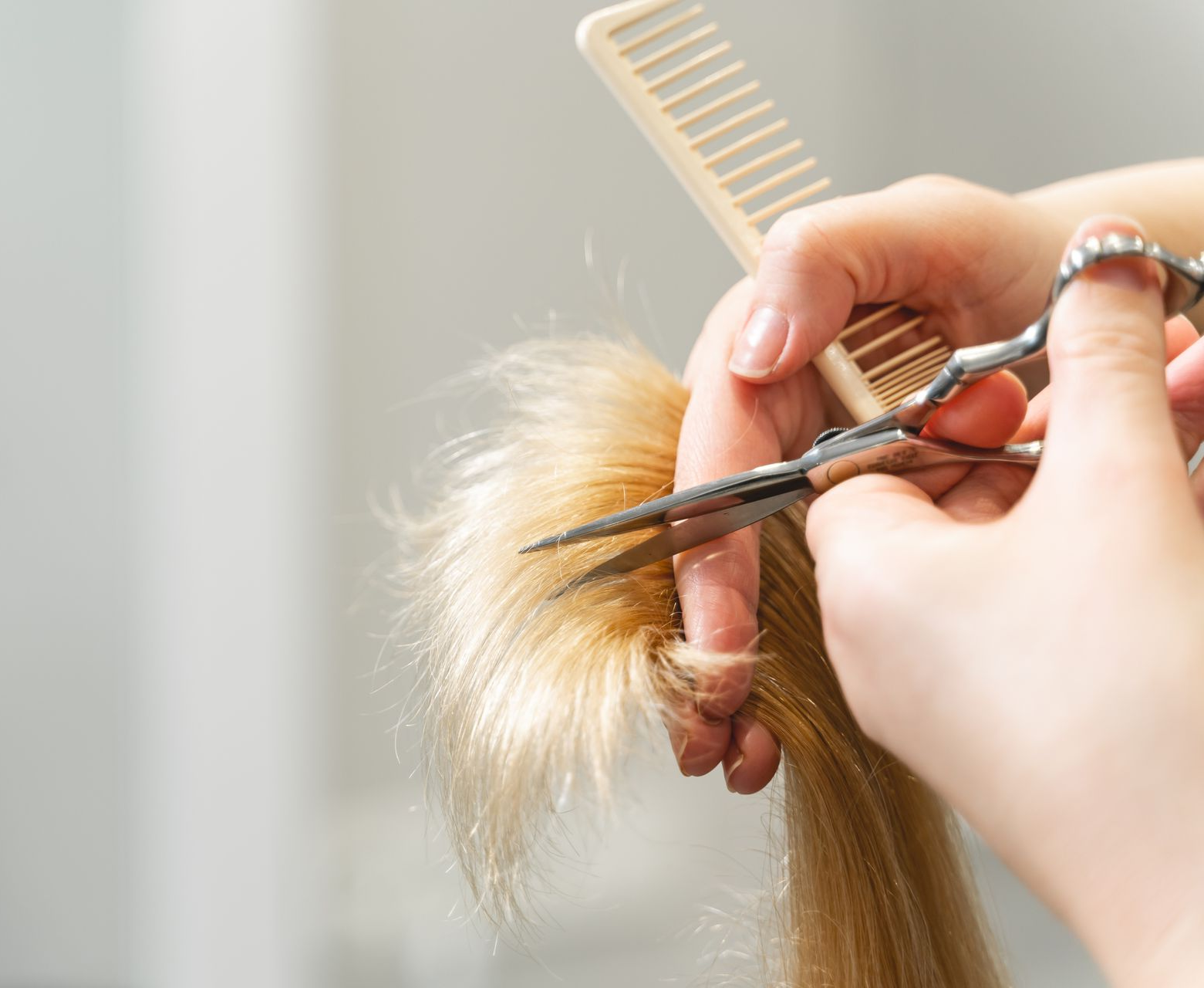 Mains tenant un peigne, des ciseaux et une mèche de cheveux blonds