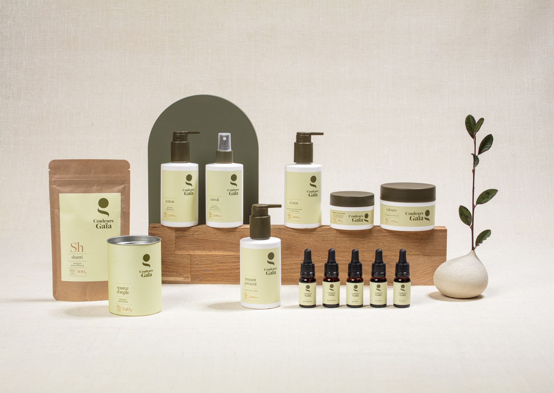 Flacons et pots de soins pour les cheveux Couleurs Gaïa, disposés sur des blocs de bois avec une branche feuillue.