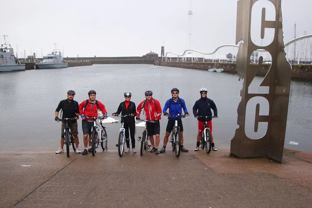Six people on bikes at a harbor, some wearing red jackets. Sign with