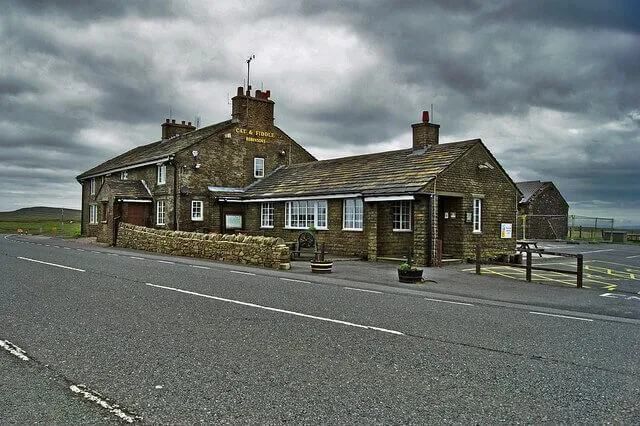 A stone pub on a roadside under a cloudy sky.