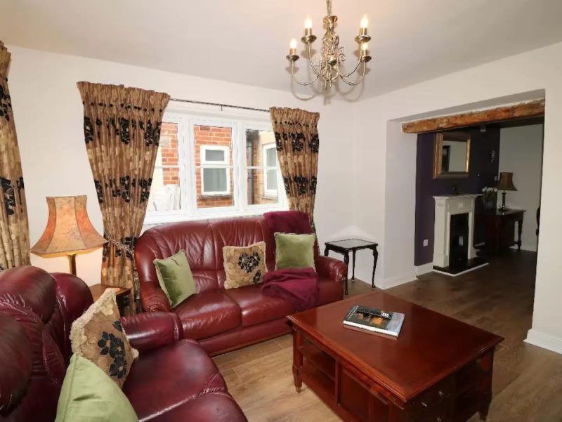 Living room with leather furniture, patterned curtains, chandelier, and a view into another room.