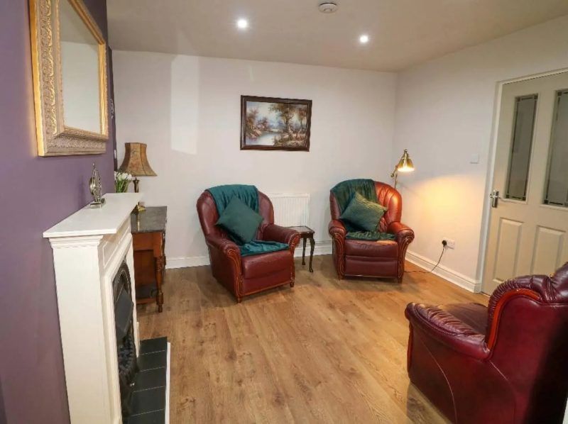 Living room with red leather armchairs, fireplace, artwork, and hardwood floors.