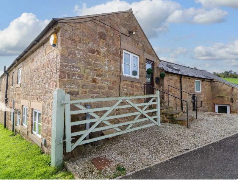 Stone cottage with a green gate and gravel driveway.