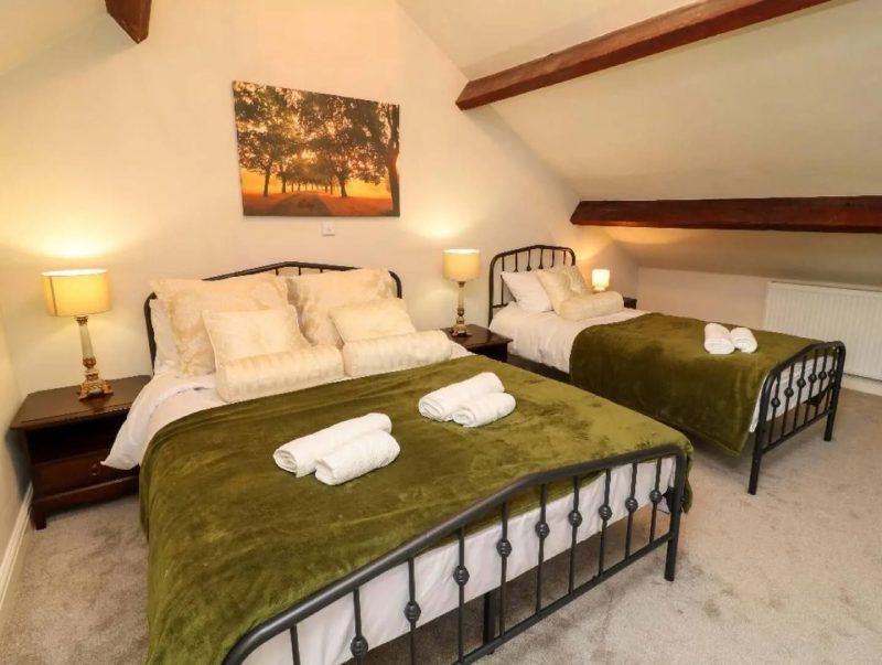 Bedroom with two beds, green blankets, lamps, and a painting on the wall.