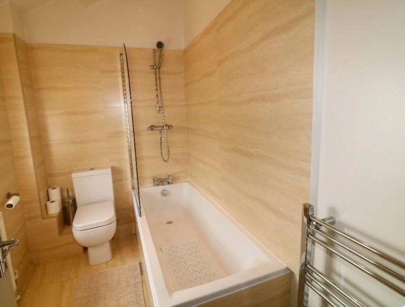 Bathroom with beige tiled walls, white toilet, bathtub with a shower and a towel rack.