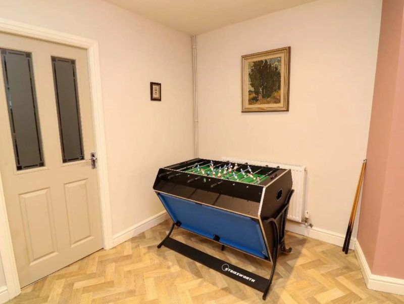 Foosball table in room with door, small framed art, and wood floor.