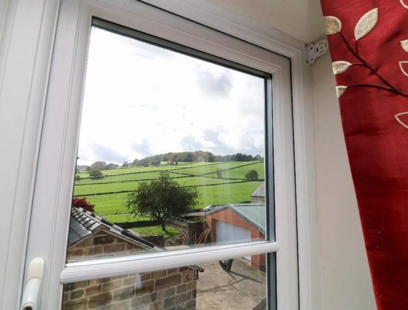 View through a white-framed window of green hills and a cloudy sky. Red curtain on the right.