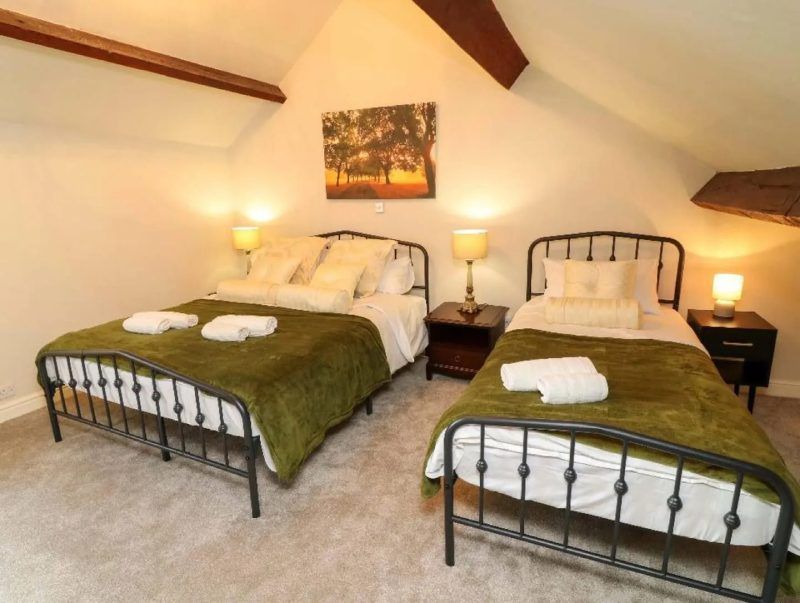 Bedroom with two beds, green blankets, and bedside lamps.